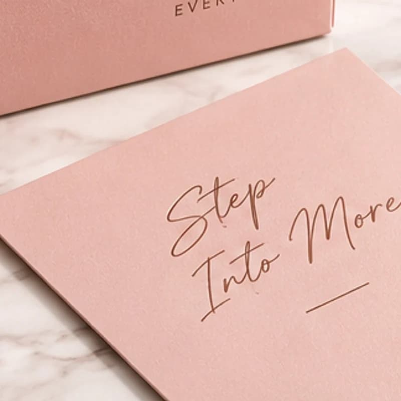 A blush Shoeelo card with 'Step Into More' in rose-gold script